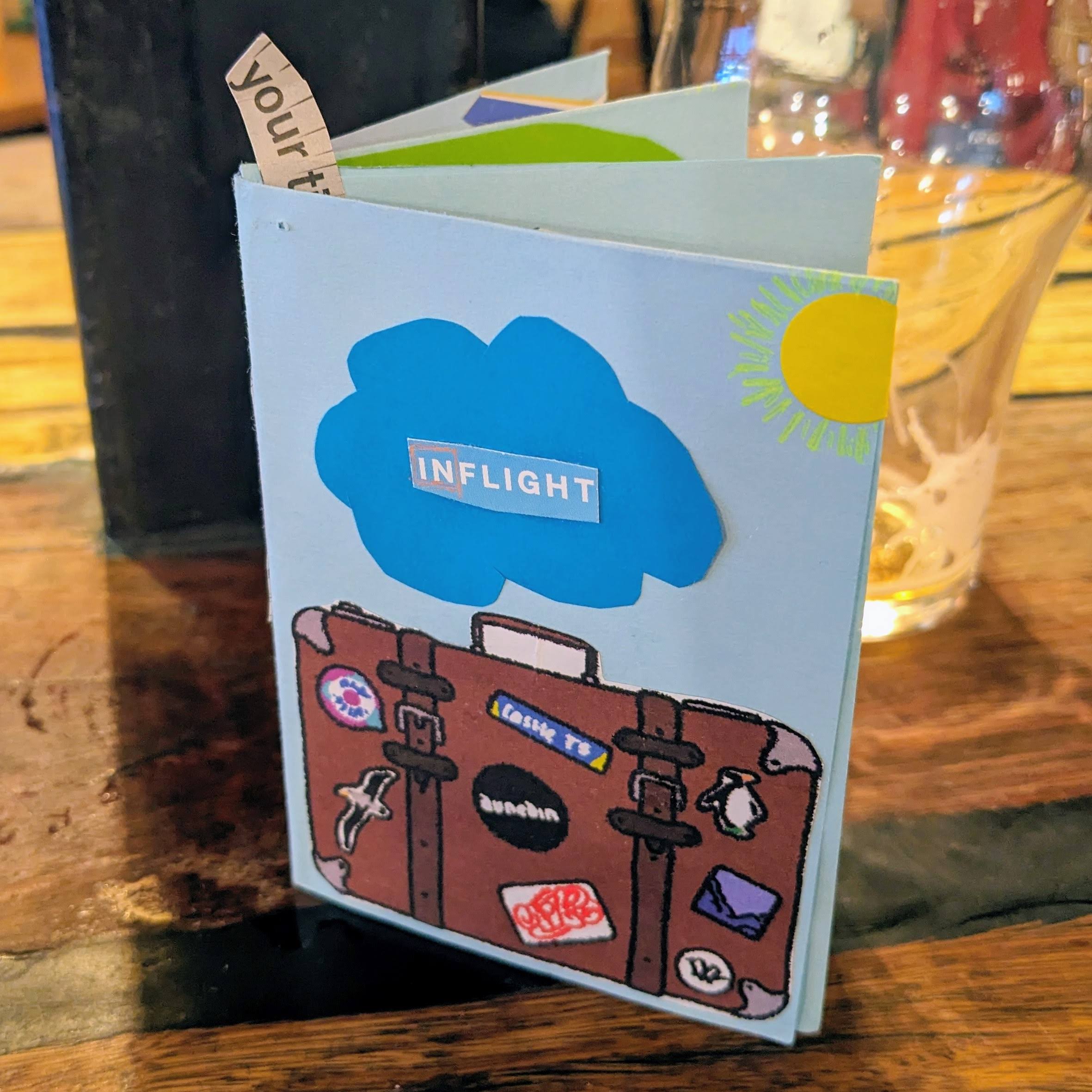 Jackson's zine INflight made at Dunedin Writers and Readers Festival 2025, showing sun, cloud and suitcase on cover